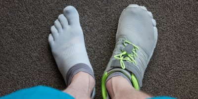 Pohled shora na chodidla, jedno v ponožce, druhé v barefoot tenisce.