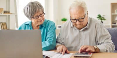 Dva důchodci si u stolu přepočítávají něco pomocí kalkulačky.