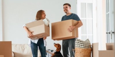 Mladý pár se stěhuje, v rukou má krabice a pod nohama psa