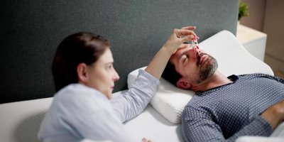 Žena dává muži v posteli kolíček na nos