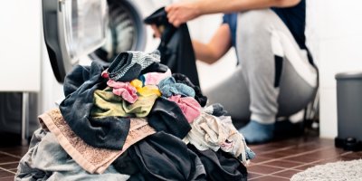 Hromada prádla a v pozadí muž s kouskem oblečení v rukou