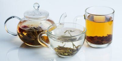 Konvička a dva čajové šálky, každý s čajovými lístky a jiným čajovým nálevem