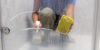 Žena umývá skvrny od tvrdé vody na dveřích od sprchového koutu