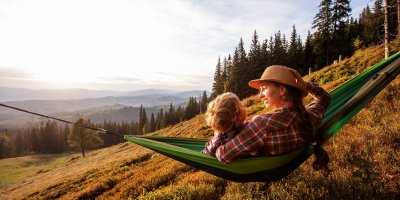 Žena s dítětem sedící v houpací síti v přírodě s výhledem na kopce