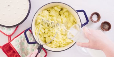 Bramborová kaše v hrnci, ke které člověk přilévá mléko.