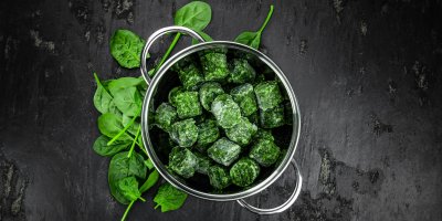 Mražený špenát v kastrolu, listy čerstvého špenátu vedle