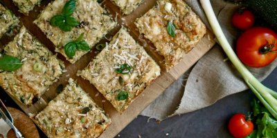 Cuketový nákyp na dřevěném prkénku, kolem rajčata a jarní cibulka