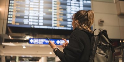 Žena s batohem čeká na spoj před tabulí s odlety