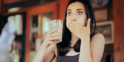 Žena v ruce drží sklenici sody a druhou rukou se drží za ústa