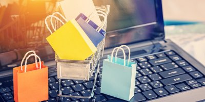 Malý nákupní vozíček a tašky položené na klávesnici počítače.