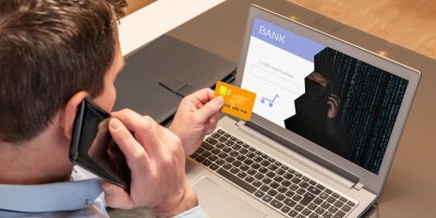 Muž telefonuje před svým laptopem a v ruce drží platební kartu.