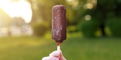 Ruka drží čokoládový nanuk, příroda v pozadí