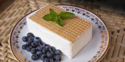 Krémová zmrzlina s oplatkou lístkem máty na vrchu, vedle hrst borůvek