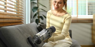 Žena vysává ručním vysavačem čalounění pohovky.