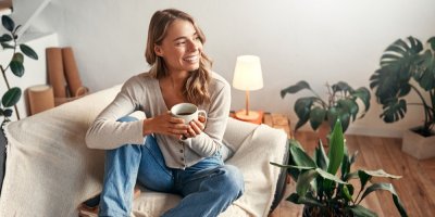 Mladá žena sedí na gauči s hrnkem kávy