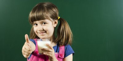 Holčička drží v ruce sklenici s mlékem a ukazuje palec nahoru