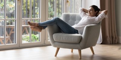 Žena sedí na gauči s nohama nahoře a rukama za hlavou.