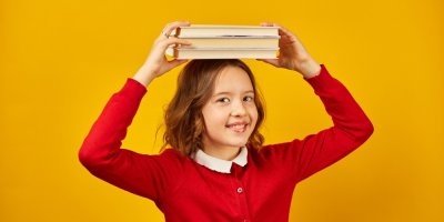 Školačka v červeném svetru drží na hlavě tři knihy