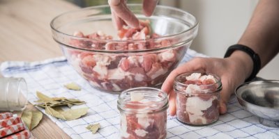 Muž plní sklenice syrovým masem nakrájeným na kostky.