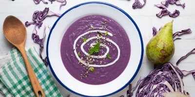 Fialová mixovaná polévka zdobená semínky a zakysanou smetanou servírovaná v bílém talíři