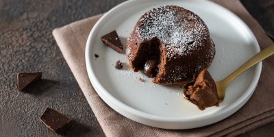 Čokoládové suflé nakrojené lžičkou, z jeho středu vytéká čokoládová náplň.