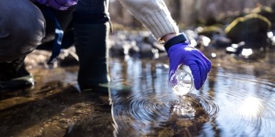 Nabírání vody z potůčku ve fialových rukavicích