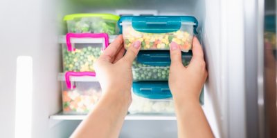 Ruce vkládající plastové krabičky do lednice s rozličnými potravinami v plastových dózách