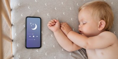 Miminko spí vedle telefonu pouštějícího uklidňující zvuky pro spánek.