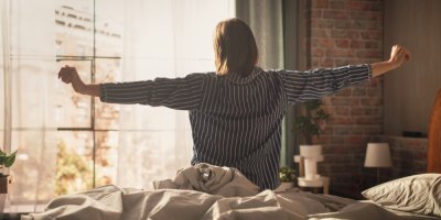 Žena se protahuje na posteli před oknem