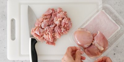 Syrové kuřecí maso nakrájené na plastovém prkénku, položený nůž a ruce drží krabičku s masem v celku