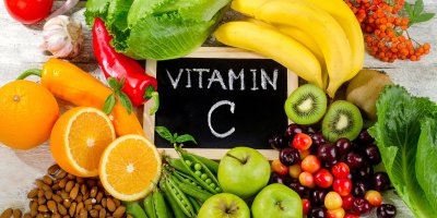 Tabulka s nápisem Vitamin C, kolem jsou pomeranče, papriky, mandle, hrášek, třešně, jablka, kiwi, salát, banány, česnek