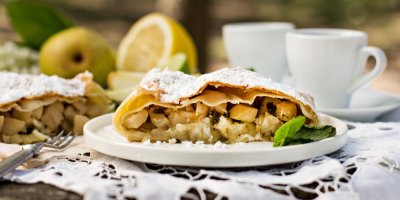 Štrúdl na talířku a v pozadí dva šálky a citron