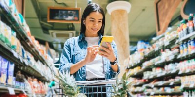 Žena nakupuje v obchodě a dívá se do telefonu