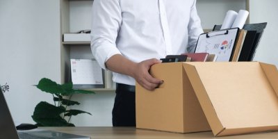 Muž v košili si v kanceláři balí krabici se svými věcmi