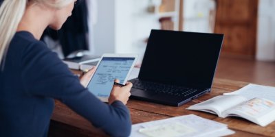 Žena si dělá poznámky na tabletu před notebookem