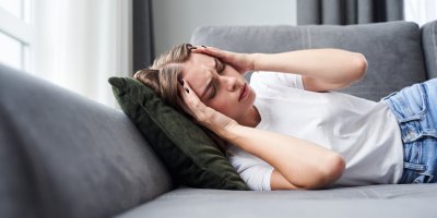 Žena s bolestí hlavy ležící na gauči