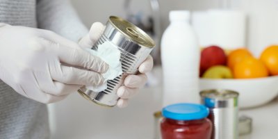 Osoba v rukavicích pečlivě čistí plechovku.