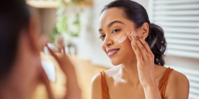 Žena si před zrcadlem nanáší na obličej krém.