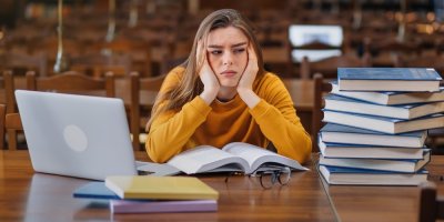 Dívka sedí mezi knihami a notebookem a tváří se znuděně