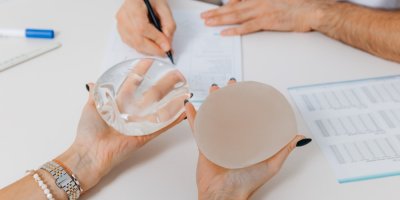 Žena drží v ruce 2 prsní implantáty