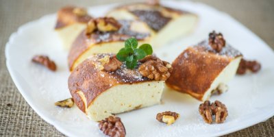 Tvarohový koláč posypaný vlašskými ořechy na bílém talířku