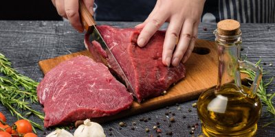 Záběr na ruce krájející červené maso