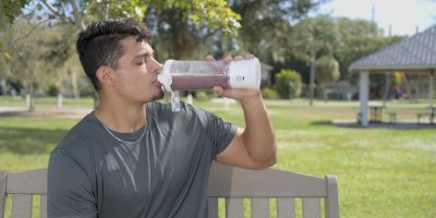 Muž na lavičce pije smoothie z přenosného mixéru.