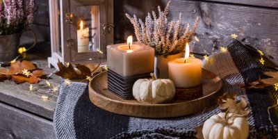 Pléd, na kterém je tác se svíčkami, vřesem a dekorační dýní, kolem jsou světýlka, listy a lucerna