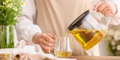 Člověk nalévá heřmánkový čaj z konvice do hrnku