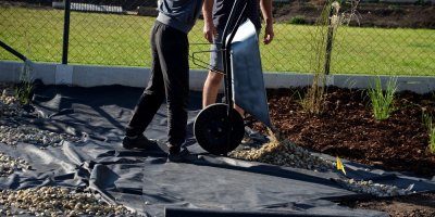 Černá geotextilie umístěná pod kůrou a štěrkem na zahradě