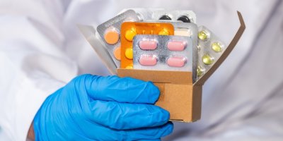 Ruka v modré rukavici drží krabičku s různými léky
