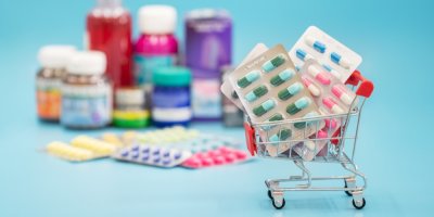 V pozadí léky, v popředí malý nákupní vozík s léky
