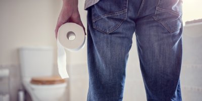 Muž stojí před záchodem a drží v ruce toaletní papír