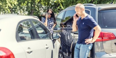 Muž a žena telefonují a stojí vedle aut